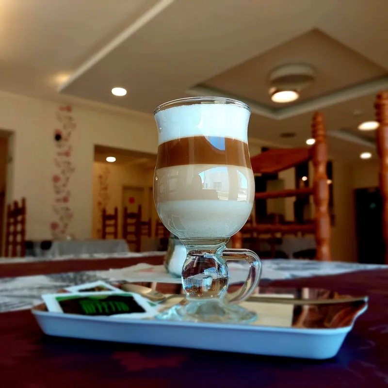 Latte macchiato egy tálcán, háttérben a világos terem faragott székeivel